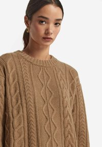 Kabelstrickpullover in einer sanften, tanfarbenen Nuance. Mit strukturierten Mustern und Rundhalsausschnitt. Aus gemütlichem Strickmaterial gefertigt.
