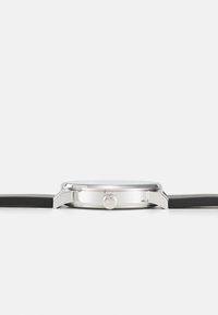 Reloj de acero inoxidable plateado con correa de caucho negra. Presenta una caja redonda, un bisel liso y una corona para ajustar la hora.