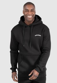 Haut à capuche noir en tissu doux, avec une poche kangourou, des cordons de serrage et un petit logo blanc sur la poitrine. Design à coupe régulière.