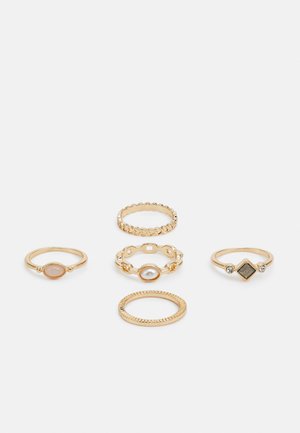 Conjunto de cinco anéis dourados com designs variados: um com uma pedra oval, um com uma banda texturizada e vários com acentos decorativos.
