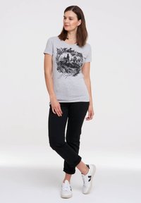 Gray cotton t-shirt with a black graphic print featuring a cityscape within a floral border. Paired with black pants and white sneakers.