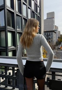 Svjetlosiva, uska dugih rukava i crne kratke hlače. Gornji dio ima glatku teksturu; odjeća je dizajnirana s krojem koji je skraćen i usklađen uz tijelo.