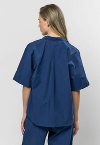 Tumedat sinine lühikeste varrukatega särk kraega, mis on loodud vabalt istuvaks ja varustatud selja voldiga, et tagada mugav liikumine, valmistatud kerge materjalist.