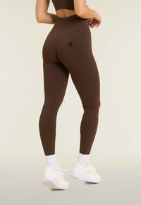 Leggings marroni a vita alta realizzati in materiale elasticizzato, con un dettaglio del logo sul retro e una silhouette liscia e aderente.