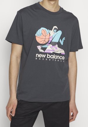 Personne portant un t-shirt gris foncé avec un graphisme coloré d'un joueur de basket-ball en dessin animé et le texte "new balance basketball" à l'avant.