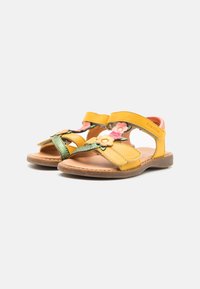 Gelbe Leder-Sandalen mit floralen Akzenten, verstellbaren Riemen und einer braunen Sohle. Merkmale sind grüne und rosa dekorative Elemente.
