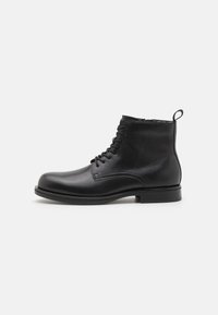 Bottes de cheville en cuir noir avec un bout arrondi, un système de laçage à l'avant et une petite languette à l'arrière. Semelle plate et texture lisse.