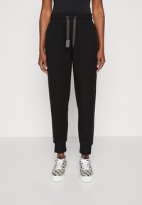 Melnas sporta bikses ar brīvu piegājienu, ar auklām, sānu šuvju akcentiem un rievotām piedurknēm. Apvienotas ar rakstainiem sporta apaviem.