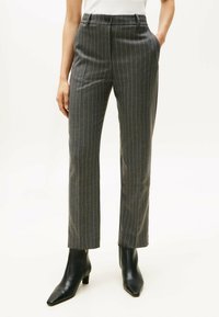Pantaloni grigi a righe sottili con una vestibilità su misura, dotati di vita media, passanti per cintura e due tasche laterali. Completati da stivaletti neri alla caviglia.