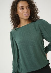 Grüne Bluse mit einem strukturierten, gestreiften Design und leichtem Glanz. Sie hat einen runden Ausschnitt und lange Ärmel mit gerafften Akzenten.