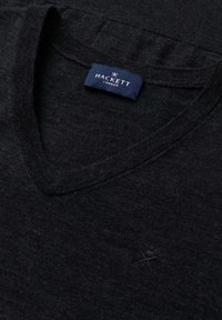 Zwarte v-hals trui van een gestructureerde stof met een subtiele geborduurde logo op de borst en een marineblauwe label op de halslijn.