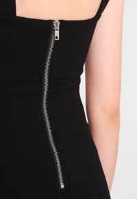 Svart klänning med ett bakre silverblixtlås, slätt tyg, figursydd design och tunna band, som visar upp en ren och minimalistisk stil.