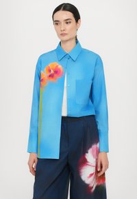 Light blue shirt with long sleeves, featuring vibrant floral prints in orange and pink; includes a chest pocket and button-down style.