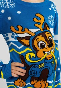 Maglione lavorato a maglia blu con un cane dei cartoni animati con corna e una sciarpa gialla, decorato con fiocchi di neve e motivi in colori contrastanti.
