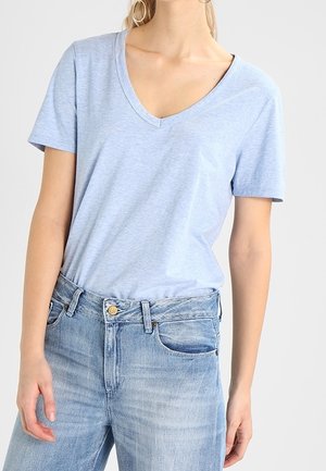 Donna che indossa una maglietta azzurro chiaro a maniche corte con scollo a V infilata in jeans blu sbiaditi a vita alta con bottone e passanti per cintura.