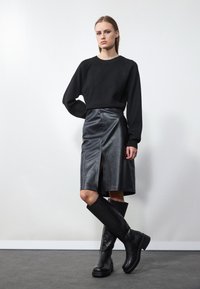 Black knit sweater paired with a black leather midi skirt featuring a front slit. Knee-high black leather boots with a chunky sole.