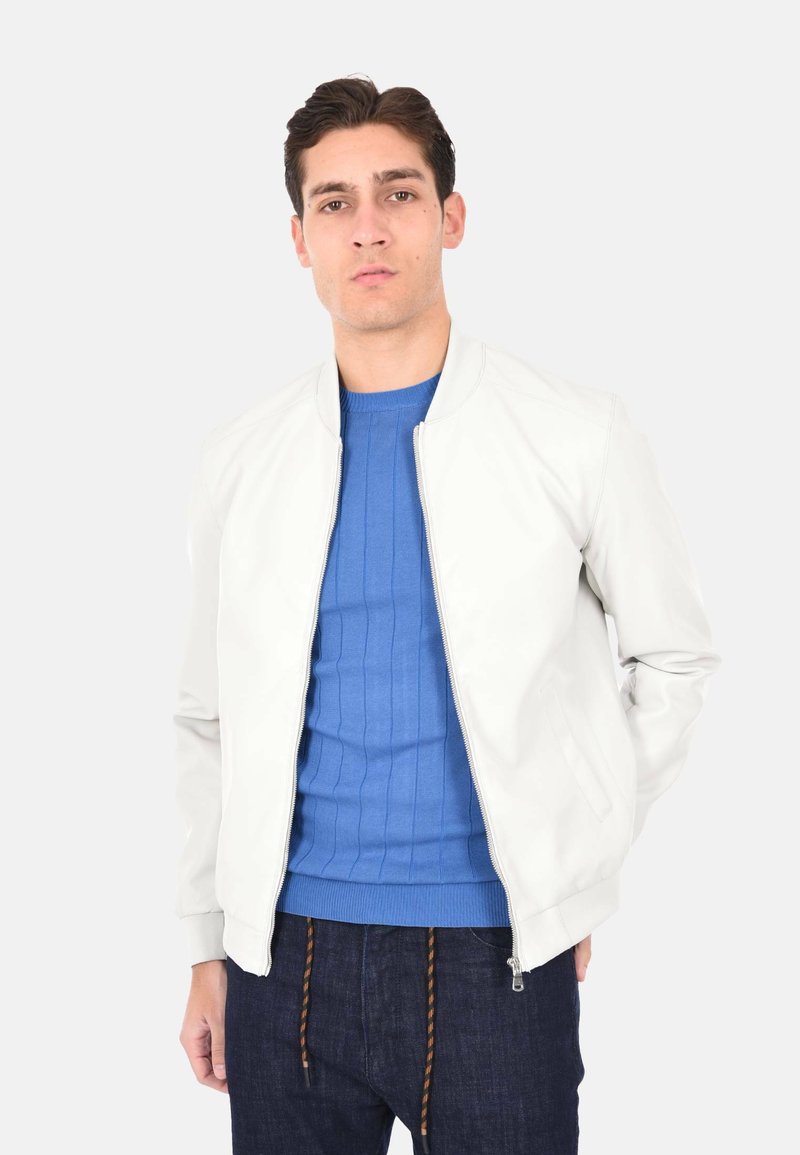 Giacca bomber leggera in pelle bianca con colletto rialzato, chiusura frontale con zip e tasche laterali, indossata sopra un maglione blu a coste.