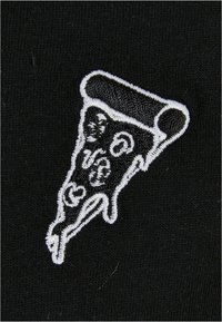 Černá látka s bílou vyšitou podobiznou plátku pizzy, s detailními přísadami a zakřiveným okrajem kůrky.