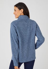 Chaqueta de forro polar en un azul marino jaspeado con cuello alto, mangas largas y un corte holgado. Textura suave y diseño casual.