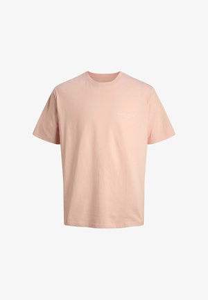 Chłopiec w jasnoniebieskiej czapce, różowej koszulce, dżinsowych szortach, białych skarpetkach i białych trampkach, stoi na tle jednolitego tła.