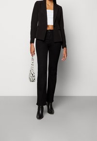 Czarna marynarka z klapami, krótka biała bluzka, rozszerzane czarne dżinsy i czarne botki za kostkę. Dodatki to torebka w paski zebra.