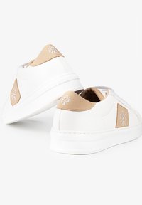 Zapatillas blancas con acentos de gamuza beige y logotipo. Presentan una suela plana, cierre con cordones y un collar acolchado. Material suave en todo el zapato.
