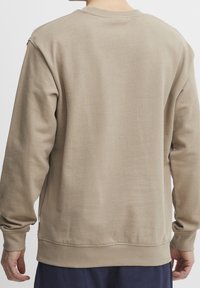 Sweat-shirt marron clair, mélange de coton, encolure ronde, poignets et ourlet côtelés, design simple, texture douce, coutures minimales, vue de dos.