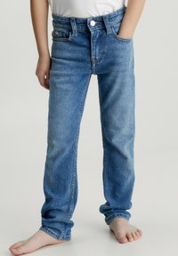 Jeans de mezclilla azul con corte recto, cierre de botón y cremallera, cinco bolsillos y ligero desgaste en la tela, enrollados en los puños.