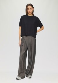 Zwart gebreid cropped t-shirt met korte mouwen, gecombineerd met grijze gestreepte brede broek. Model draagt zilveren sneakers.