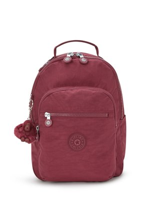 Maroon nylon backpack with zippered compartments, logo patch, and a furry monkey keychain attached to the zipper pull.