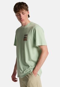 Ανοιχτό πράσινο βαμβακερό T-shirt με άνετη εφαρμογή, που διαθέτει τετράγωνο λογότυπο στο στήθος. Κοντά μανίκια και στρογγυλή λαιμόκοψη.