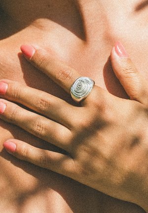 Hand with pink polished nails wearing a silver textured ring resting on a bare shoulder under soft natural light.