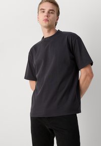 Camiseta negra de algodón de mangas cortas y escote redondo. Presenta un pequeño logo en el cuello y tiene un corte relajado.