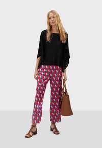 Černý volný top, barevné geometrické kalhoty v červené, růžové a modré barvě. Hnědá kabelka a hnědé sandály na pásky.