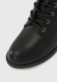 Czarny skórzany but z zaokrąglonym czubkiem, sznurowaniem i metalowymi oczkami. Gładka faktura, solidna konstrukcja i minimalistyczny styl.