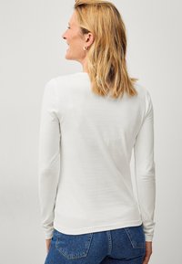 Witte langekousen shirt met een getailleerd ontwerp, gladde textuur en een ronde halslijn, gecombineerd met blauwe denim jeans.