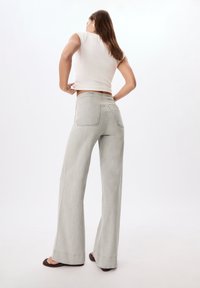 Jeans gris clair à jambes larges en denim. Présente deux poches arrière et une taille haute. Associé à un haut blanc ajusté et des sandales.