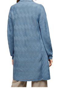 Lungo cappotto blu realizzato in tessuto testurizzato con un motivo ondulato, dotato di colletto e maniche lunghe. Presenta slit laterali per facilitare i movimenti.