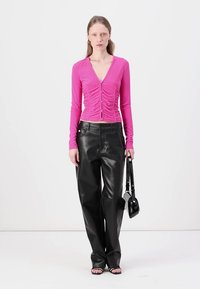 Fitted pink long-sleeve top with gathered front and buttons, paired with loose black leather pants and a small black handbag.