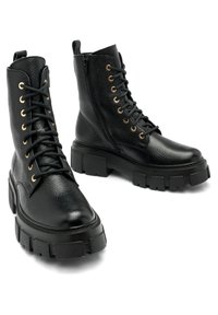 Botas negras de cuero hasta el tobillo con acabado texturizado. Presentan cordones en la parte delantera, ojetes dorados, cremallera lateral y suela gruesa de goma.