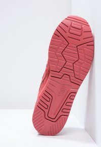 Röd gummisneaker-sula med ett strukturerat greppmönster och en vinklad vy som visar djupa spår för grepp och hållbarhet.