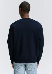 Sudadera de cuello redondo en azul marino, con mangas largas, puños y dobladillo de canalé. Textura de tela suave, diseño sencillo y sin patrones ni logotipos visibles.