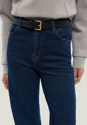 Ciemnoniebieskie dżinsy z denimu o prostym kroju, zestawione z czarnym skórzanym paskiem z złotą klamrą. Gładka faktura, minimalne zdobienia.