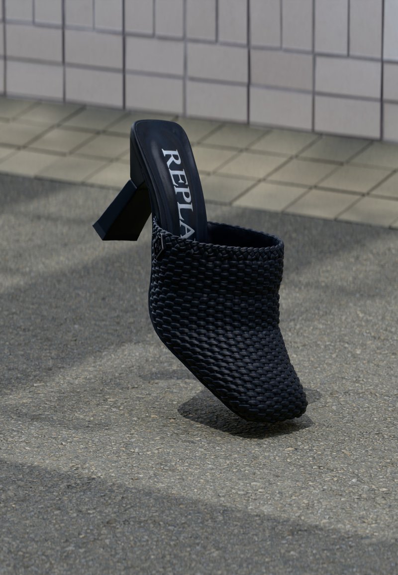 Μαύρο υφαντό mule με τακούνι, τετράγωνη μύτη και χοντρό τακούνι, με την επιγραφή "REPLA" στο εσωτερικό, τοποθετημένο σε εξωτερική επιφάνεια με πλακάκια και άσφαλτο.