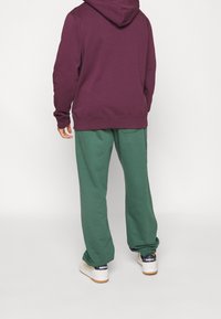 Vinröd huvtröja och gröna mjukisbyxor. Blandat bomullstyg, lös passform, elastiska mudd och midjeband. Sneakers med vita sulor.