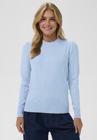 Ljusblå stickad tröja med långa ärmar, rund halsringning, ribbad fåll och puffade axlar. Bärs tillsammans med mörkblå byxor.