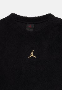 Μαύρη φλις μπλούζα Jordan με κεντημένο λογότυπο Jumpman σε χρυσό στο στήθος και μαύρη ετικέτα μέσα στον γιακά.