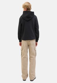 Sweatshirt à capuche noir avec une coupe décontractée, associé à un pantalon cargo beige avec des poches latérales et une coupe droite, porté avec des baskets.