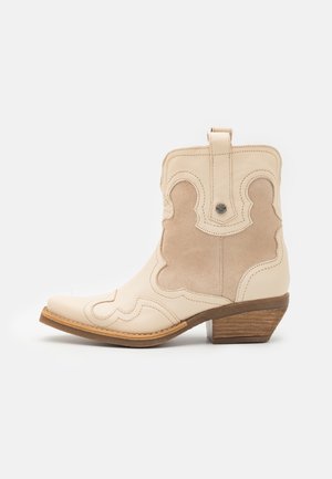 Cremefarbener und beiger Cowboystiefel mit dekorativer Naht, Zuglasche und gestapeltem Holzabsatz auf weißem Hintergrund.
