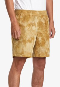 Tan tie-dye shorts made of soft fabric, featuring an elastic waistband and a relaxed fit, designed for comfort and casual wear.